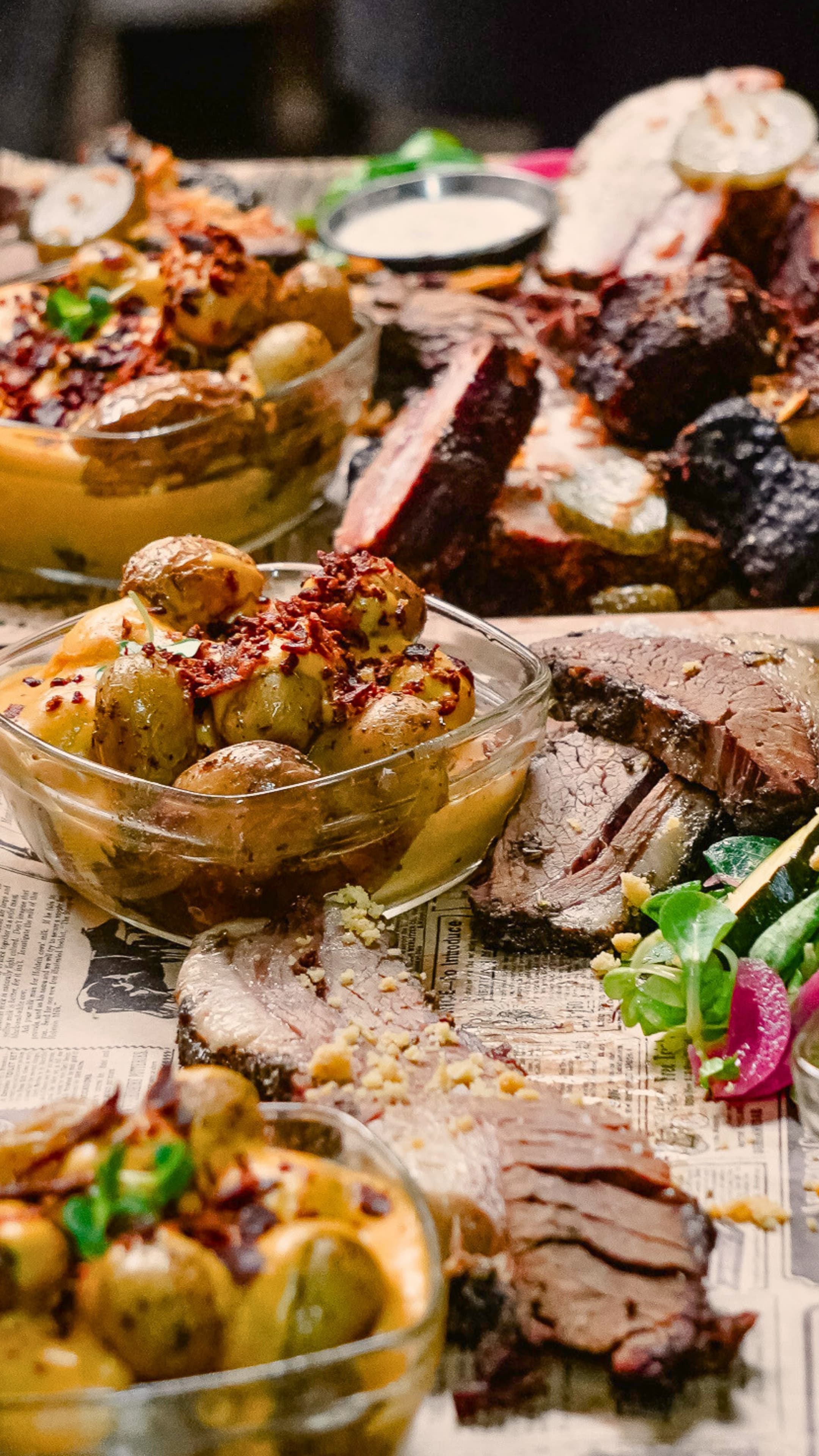 Grande tablée de viandes fumées tranchées, grenailles et sauces servies à partager sur papier journal